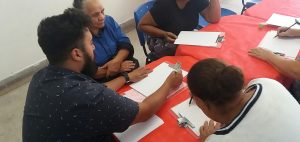 pessoas sentadas a uma mesa vermelha e fazendo anotações