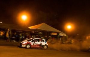 O Peugeot 208 Maxi Rally da equipe Acelera Siriema se deslocando à noite na direção esquerda da imagem, deixando um rastro de poeira por trás