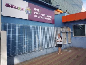 professora segurando materiais posa para foto diante da EMEF Professor Alexandrino da silveira Bueno em Barueri