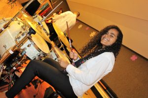 garota tocando bateria e sorrindo para a câmera