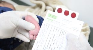 mãos de um médico ou médica que realiza o teste do pezinho em um bebê enquanto analisa os resultados