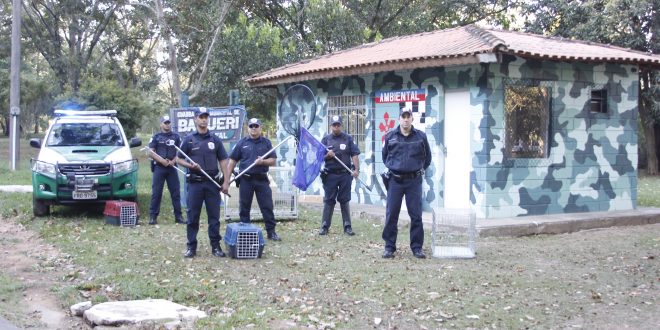 cinco homens da Guarda Ambiental de Barueri posam com armas diante do posto da corporação, com uma viatura atrás e à direita deles