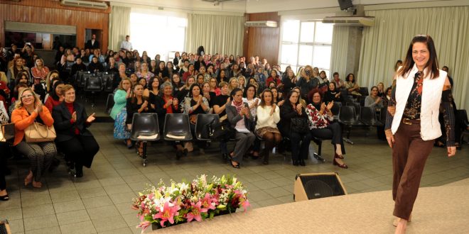 primeira-dama Lúcia França no palco, com diversas primeiras-damas e empresárias ao fundo em reunião do fundo social de solidariedade