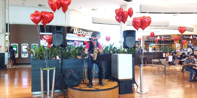 um músico se apresentando no palco da praça de alimentação do Parque Shopping Barueri com balões de corações dispostos em volta durante o Barueri Music especial de Dia dos Namorados