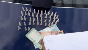 ampolas de cocaína, dinheiro e um documento de identidade dispostos numa mesa com o emblema da Guarda Civil de Barueri ao fundo