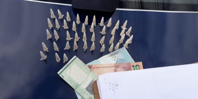 ampolas de cocaína, dinheiro e um documento de identidade dispostos numa mesa com o emblema da Guarda Civil de Barueri ao fundo