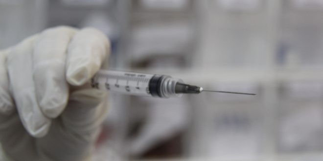 uma seringa sendo segurada por uma mão com luva médica