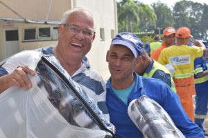 dois homens sorriem para a câmera com kits recebidos pela campanha do agasalho