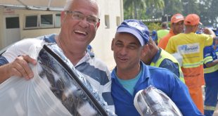 dois homens sorriem para a câmera com kits recebidos pela campanha do agasalho