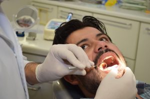 um caminhoneiro tendo sua boca examinada pelas mãos de um(a) dentista(a)