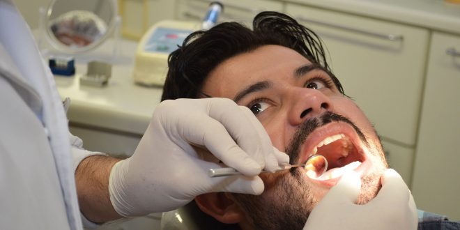 um caminhoneiro tendo sua boca examinada pelas mãos de um(a) dentista(a)