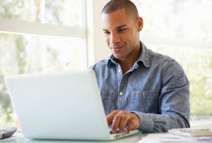 um homem sorri enquanto digita em um notebook branco