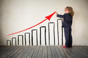 uma garotinha vestida de terno desenha uma seta vermelha acendente sobre uma fila de pilares alinhados em ordem crescente de altura