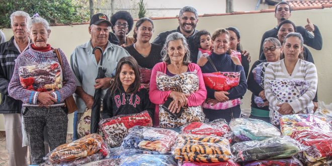 munícipes posam para foto atrás de mesa cheia de kits de doações da campanha do agasalho; alguns seguram kits que receberam