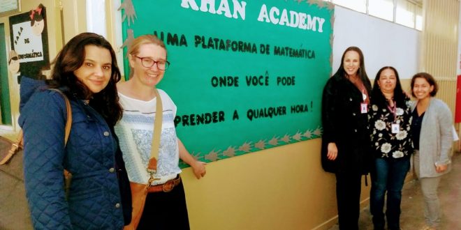 representantes posam ao lado de mural da escola com professoras