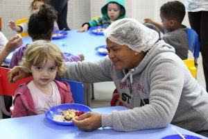 educadora dá de comer a uma criança na maternal do vale do sol