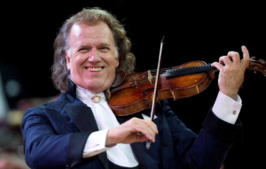 André Rieu de terno sorrindo e tocando violino