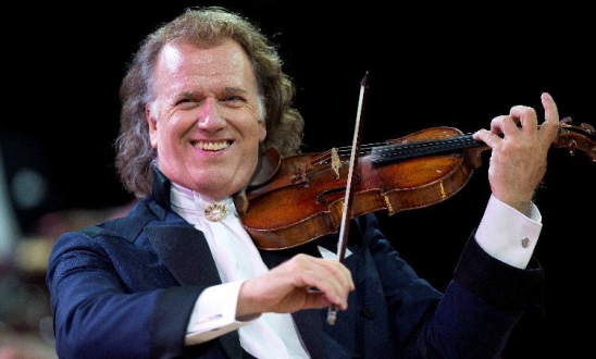 André Rieu de terno sorrindo e tocando violino