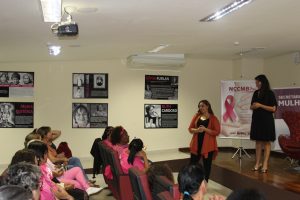 mulheres de rosa acompanham palestrantes, que estão no palco