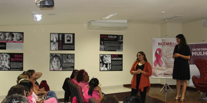 mulheres de rosa acompanham palestrantes, que estão no palco