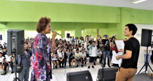 luciana melo se apresentando no palco da Emef Sidney Santucci com um músico, com o público acompanhando atrás