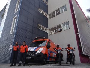 dois agentes da  defesa civil de barueri posam em suas motos ao lado de uma van do órgão com duas outras agentes posando ao lado