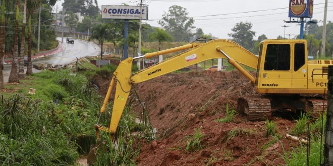 retroescavadeira revirando terra perto de córrego