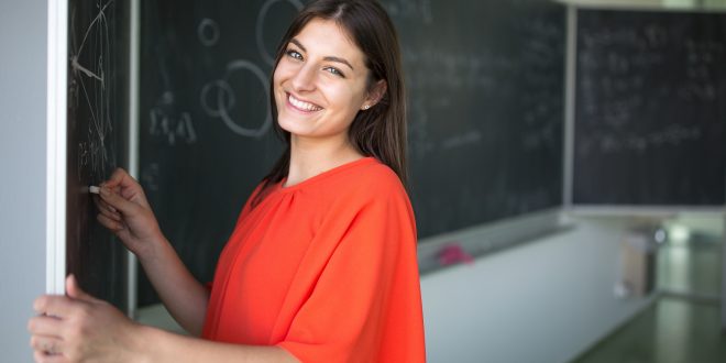 uma estudante universiaária sorri para a câmera enquanto escreve na lousa